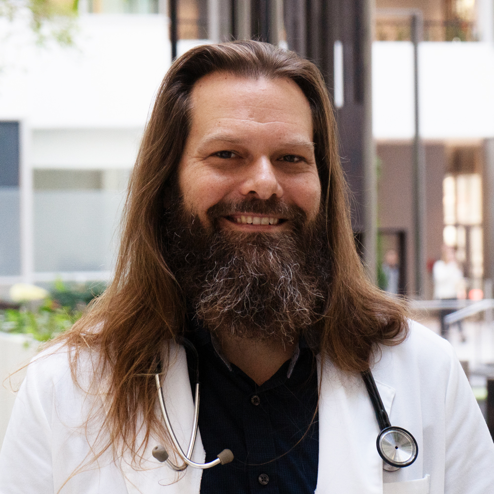 Full color headshot of Dr. Daniel Zahn, MD (aka Dr. Dan), founder of Resilient Health & Wellness, a provider of integrative medicine in Pennsylvania and New York. He has a beard and long hair, and is wearing a stethoscope with a lab coat.